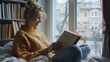 © Akmalism Photography - Young smiling woman enjoying new bestseller book sitting on window sill, happy book lover reading fiction literature relaxing at home, student teenager study textbook in modern cozy loft bedroom.