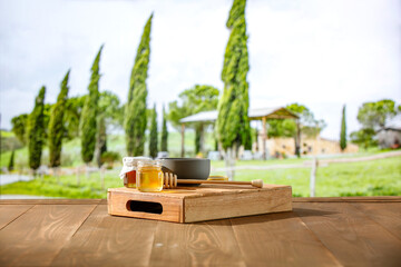 Sticker - Glass jar of honey on wooden table with nature green garden and trees Tuscany background.  Outdoor background and copy space advertising products.