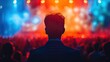 © Vodkaz - A man standing backstage at a concert, observing the vibrant and colorful lights and the crowd in front of the stage, creating a dynamic atmosphere