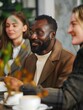 © vefimov - People sitting around a table in a modern coffee shop, engaged in conversation and enjoying each other's company.