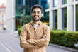 © Liubomir - Young man with glasses standing confidently outside modern office building. Smiling and crossing arms, conveying confidence and friendliness. Background features urban environment