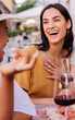 © Xavier Lorenzo - Vertical shot of two diverse women having fun enjoying aperitif with red wine sitting at an outside table in a bar. Food and beverage concept.
