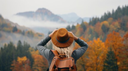 Canvas Print - A woman wearing a brown hat and a backpack is standing in a forest with trees in autumn