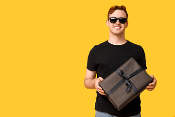 Canvas Print - Young man with gift box on yellow background. Black Friday sale