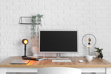 Wall Mural - Modern workplace with computer and glowing lamp near light brick wall