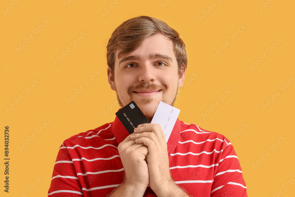 Happy young man with credit cards on yellow background