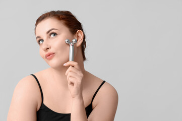 Sticker - Thoughtful young woman using facial massage tool on grey background