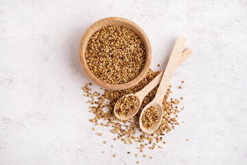 Wall Mural - Wooden bowl and spoons with raw buckwheat grains on light background