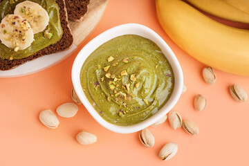 Wall Mural - bowl of tasty pistachio paste, bananas and bread pieces on orange background