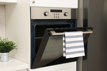 Wall Mural - Open electric oven with striped towel in kitchen. Cooking appliance