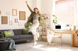 © Pixel-Shot - Young happy woman in headphones jumping and listening music in living room