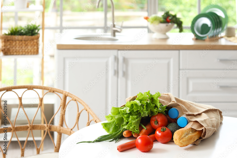 Vegetables, milk and bread in eco bag on table in kitchen
