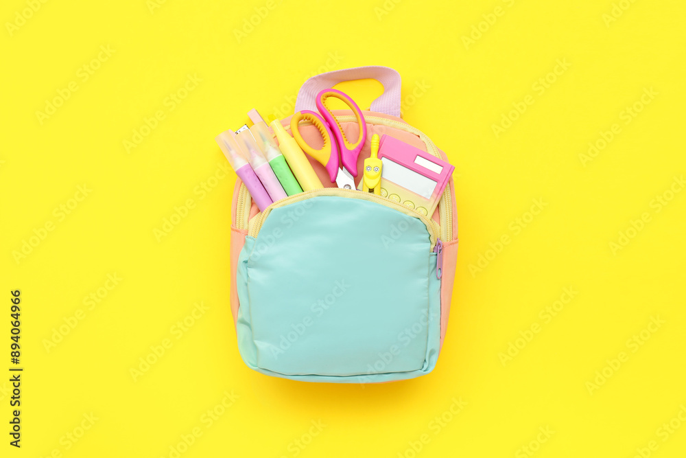 Blue school backpack with stationery on yellow background