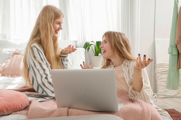 Sticker - Beautiful young happy sisters with laptop sitting on bed at home