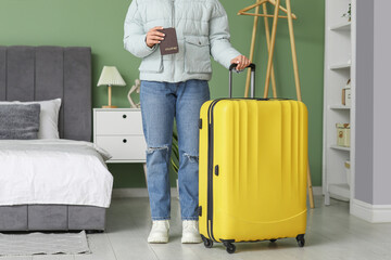 Poster - Young woman with passport and yellow suitcase at home. Travel concept