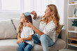 © SHOTPRIME STUDIO - Mother and daughter bonding time as they sit on a cozy couch in the living room, combing hair lovingly