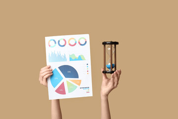 Fototapete - Female hands with financial graphics and hourglass on beige background