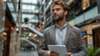 © LailaBee - Confident Businessman Holding Tablet in Modern Office Building with Glass Ceilings