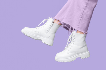 Legs of young woman in stylish white leather boots on lilac background