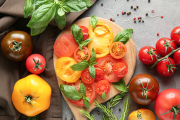 Wall Mural - Wooden board with slices of different fresh tomatoes, basil, rosemary and peppercorn on grey background