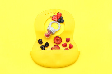 Wall Mural - Composition with baby nibbler, bib and fruits on yellow background