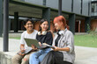 © Parichat - Group of Diverse Students Studying Outdoors with Laptops and Notebooks at Modern University Campus