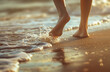 © CanvasVoyager - A close-up of barefoots walking on sand, with a blurred background of waves crashing onto a beach in summer