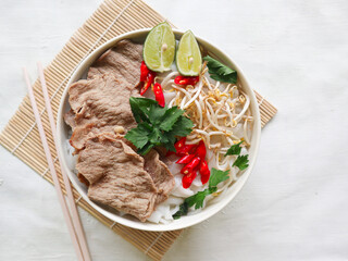 A Bowl Pho Bo traditional Soup with beef, rice noodles, ginger, lime, chili pepper in bowl. Close up. Vietnamese cuisine served on black background