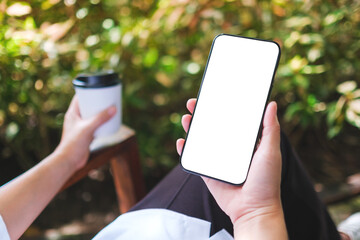 mockup image of a woman holding coffee cup and mobile phone with blank white desktop screen in the o