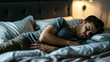 © Наталья Мирошниченко - A young man lies in bed at night holding his stomach, indicating discomfort from pain
