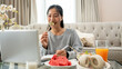 © bongkarn - A woman is eating breakfast while working or studying online on her laptop at a coffee table.