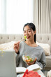 © bongkarn - A charming Asian woman is enjoying eating healthy salad at a coffee table in the living room.