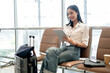 © bongkarn - A charming Asian female passenger is working remotely, using her digital tablet in the airport.