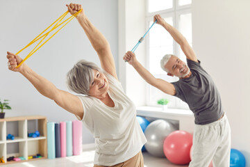 smiling mature senior man and woman doing stretching exercises with rubber band standing in gym. hap