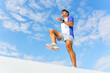 © muse studio - A man performing a high knee exercise outdoors under a clear blue sky, dressed in sporty attire.