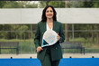 © arthurhidden - Confident businesswoman in green suit holding a padel tennis racket on a blue court. Outdoor setting with green trees in the background.