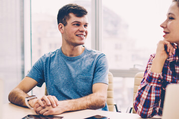 Fototapete - Cheerful male and female colleagues dressed in casual wear laughing during discussion of creative ideas sitting at meeting table in office.Positive employees talking with each other about project