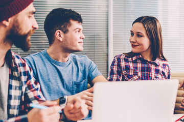 Fototapete - Cooperation of young people in casual wear on design project during brainstorming meeting in modern office.Male and female employees discussing creative idea for startup sitting at table with laptop