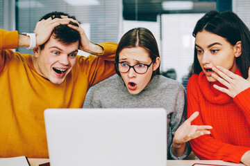 Fototapete - Amazed young people dressed in casual wear shocked with watching online broadcasting of favourite team on laptop using wireless internet.Emotional friends reading excited news in email on netbook