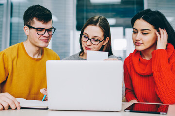 Fototapete - Successful hipster student rewriting information from business card in search job.Positive young people dressed in casual wear collaborating at laptop computer in office sitting at modern laptop