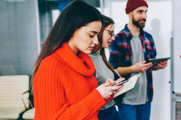 Fototapete - Group of millennial young people searching information on websites on modern gadgets during collaboration in office.Team of hipster guys with smartphone in hand discussing plan of cooperation
