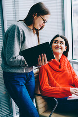 Fototapete - Hipster student consulting with successful young businesswoman which working at modern laptop computer in office.Secretary making notes in notebook while female boss checking email on netbook