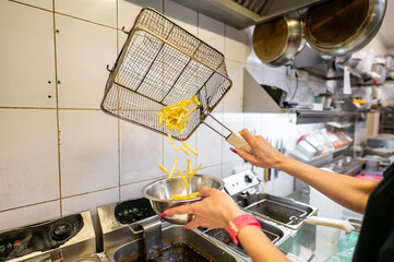 Wall Mural - Cook draining freshly fried french fries from a metal basket in a commercial kitchen.