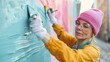 © svastix - A woman dressed in casual clothes and protective gear paints a vibrant mural on an outdoor wall, showing dedication and creativity on a sunny day.