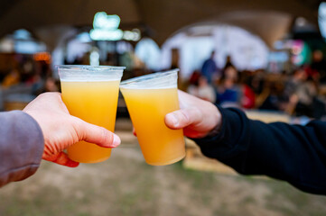 Wall Mural - Two hands clink plastic cups filled with craft beer in a celebratory toast