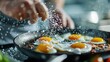 © svastix - Close-up of hands sprinkling salt on sizzling frying eggs in a black pan, capturing the essence of cooking, precision, and culinary artistry in full detail.