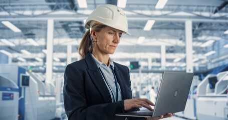 Poster - Portrait of a Happy and Smiling Caucasian Female Industrial Engineer in White Hard Hat Standing with Laptop Computer at Electronic Manufacturing Factory. Successful Employee Working Online