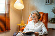 © CandyRetriever  - Happy Asian senior mature woman wearing glasses relaxing on sofa in living room and reading a book. Elderly retired grandmother enjoy indoor lifestyle with leisure activity and hobbies at home.