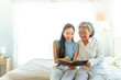 © CandyRetriever  - Happy Asian senior mature woman reading a book with caregiver in bedroom. Happy elderly woman enjoy indoor activity lifestyle at home. Senior people mental health care, nursing and caregiving concept.