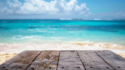 Poster - A wooden tabletop sits in front of a blurred image of a tropical beach with white sand, blue ocean, and a clear sky.